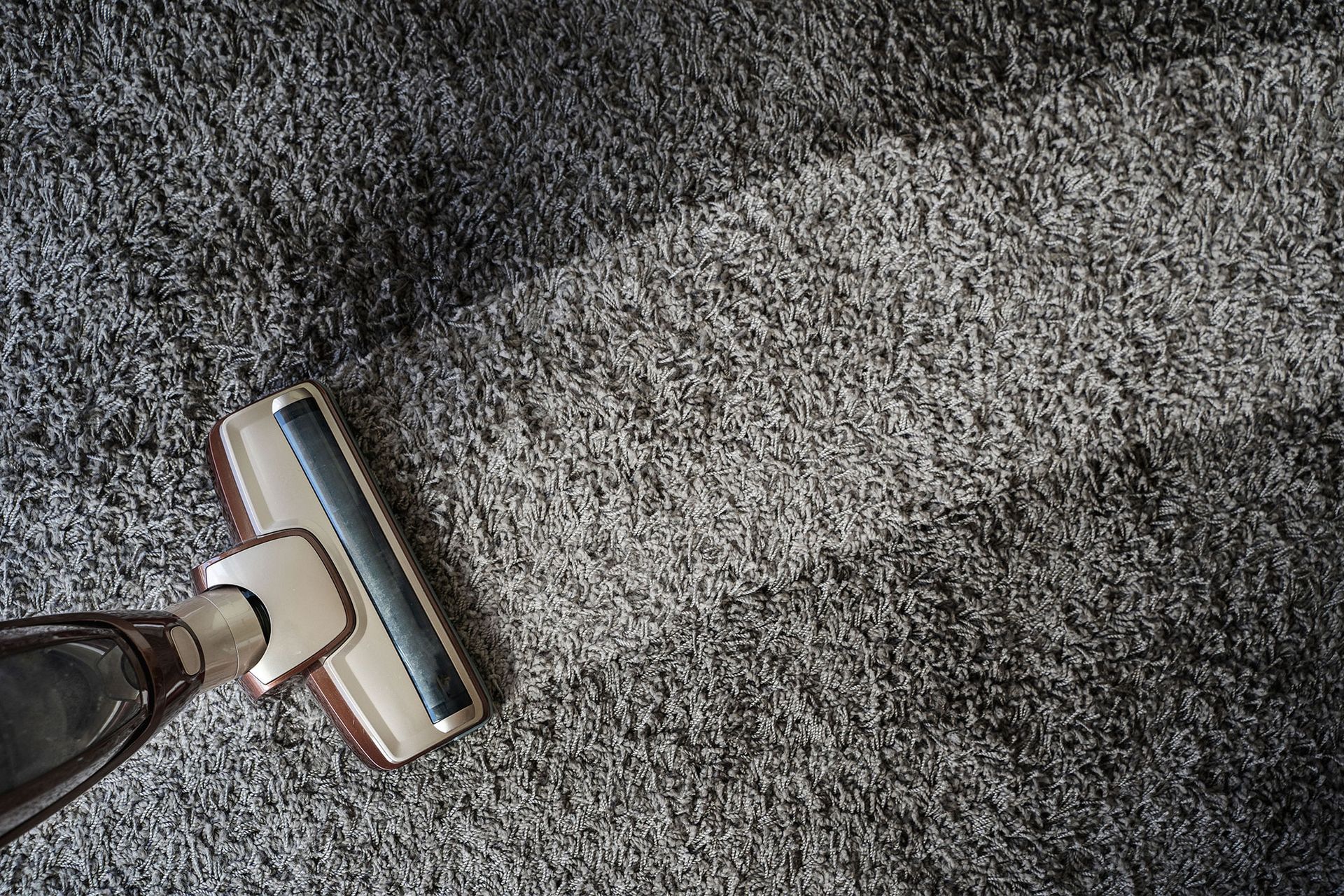 Vacuum cleaner cleaning a gray carpet, leaving a clean path.
