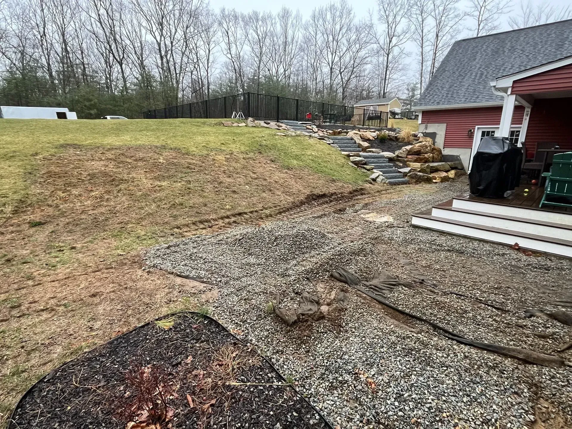 Backyard with gravel, sloped hill with steps, and a red house.
