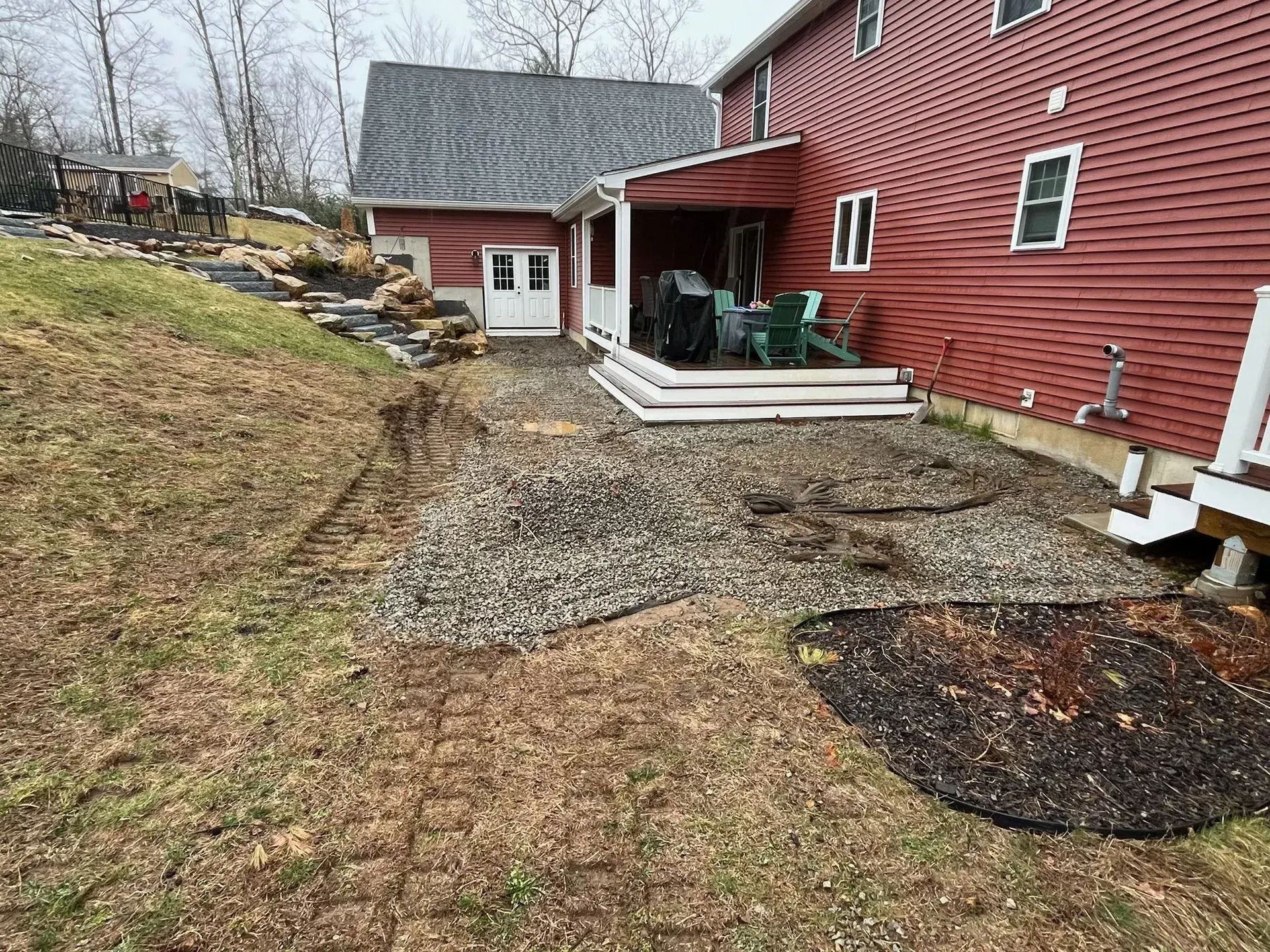 Backyard with gravel patio, red house, and a grassy hill.