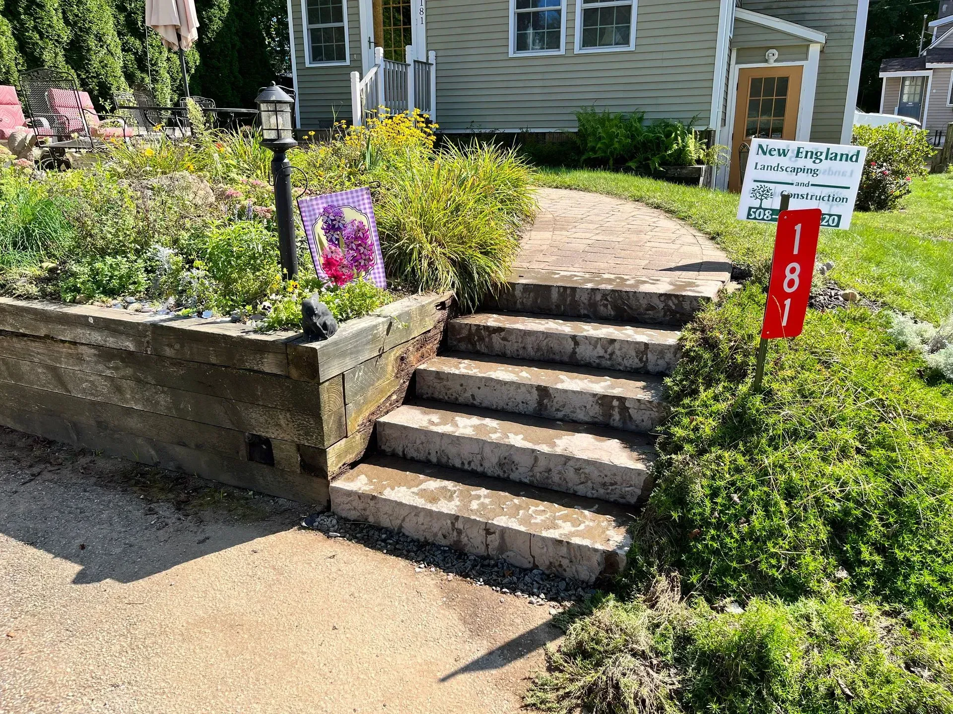 Stone steps leading up to a house with a garden bed and address sign.