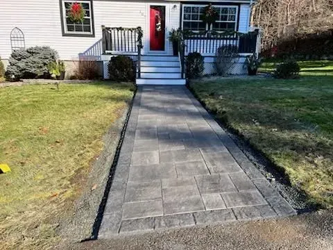 A gray paver walkway leads to the white house with a red door. Green grass surrounds it.