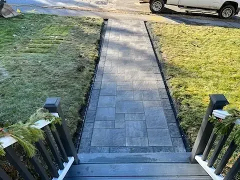 Paver walkway leading from steps to street, bordered by grass. A vehicle is partially visible.