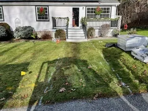 Front yard with a patchy lawn, small white house, front steps, and covered items on the right.