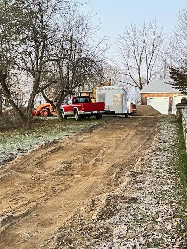 Red pickup and excavator beside a white trailer on a muddy rural driveway in winter