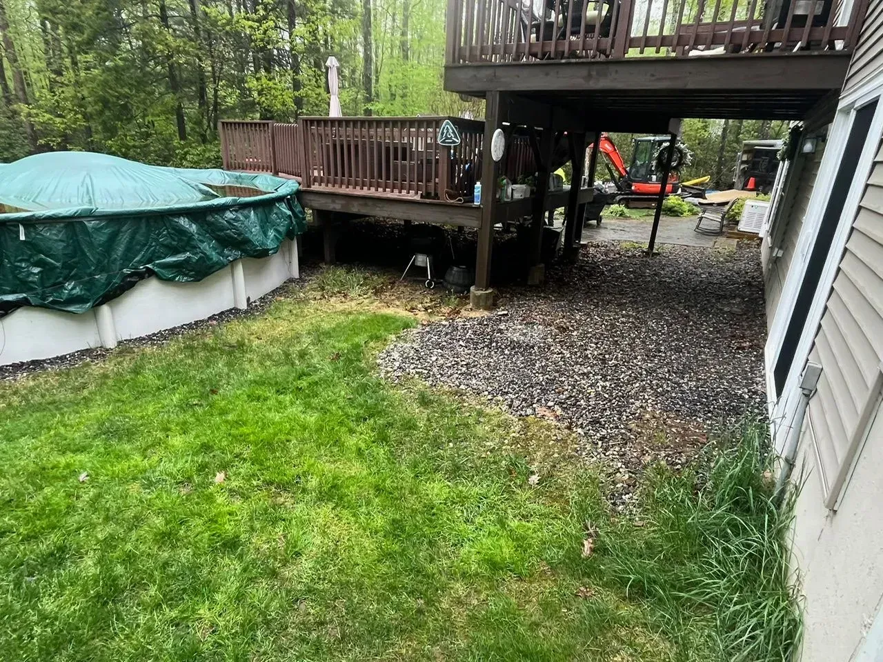 A backyard with a deck, above-ground pool, and gravel pathway next to a house.
