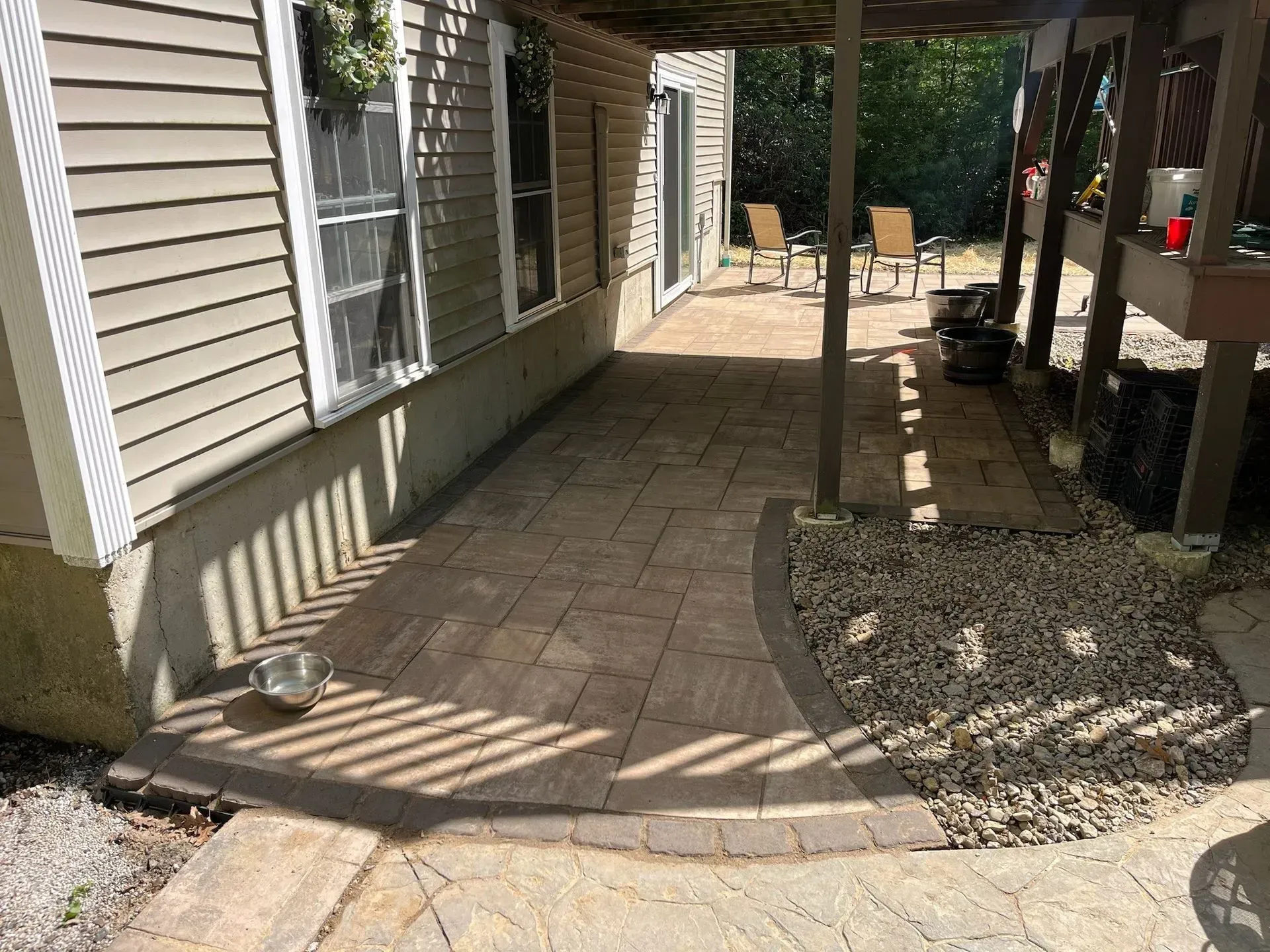 Patio with pavers under a deck, gravel border, and house siding.