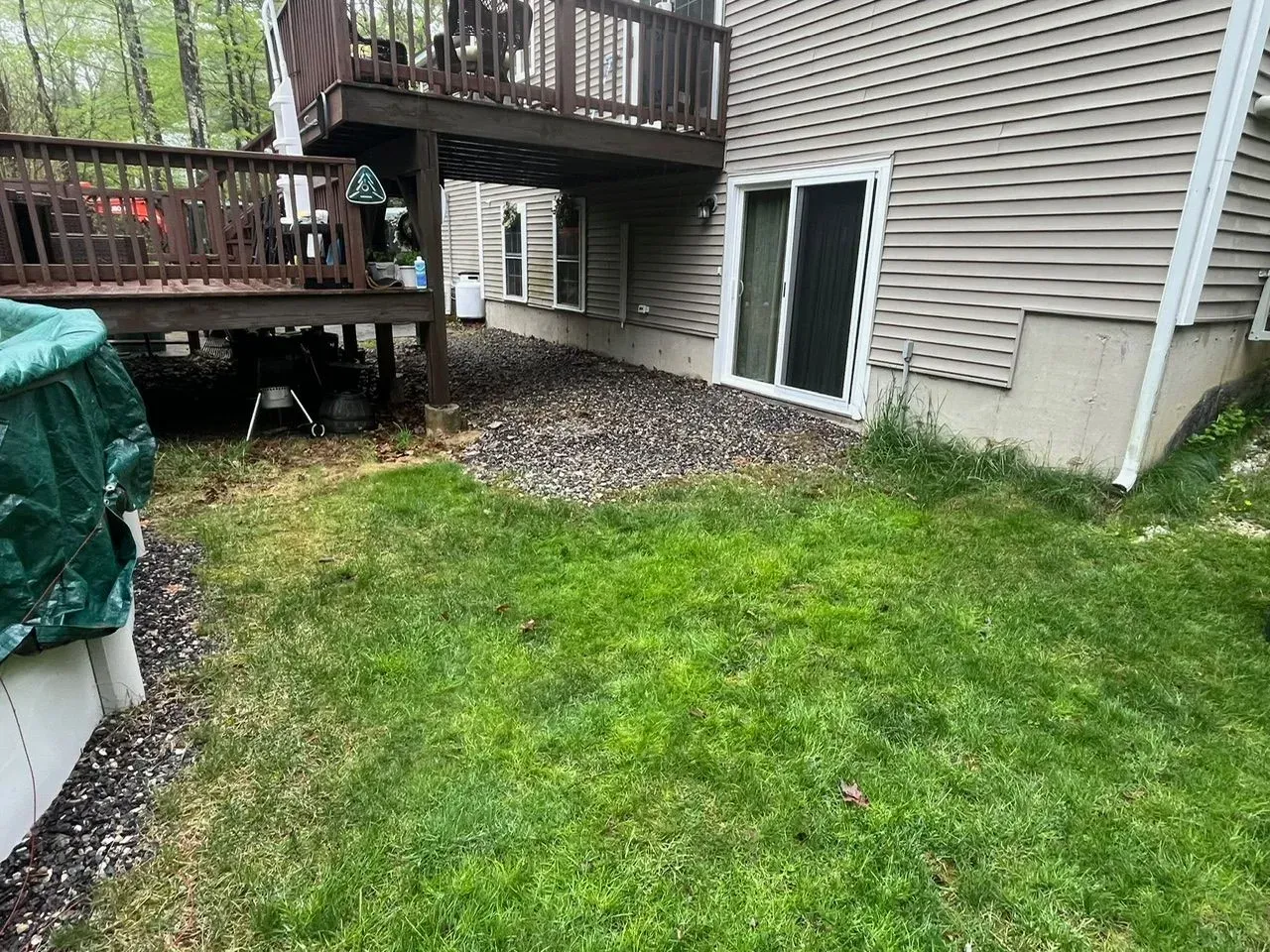 Side of house with sliding glass door, deck, and patches of grass and gravel.