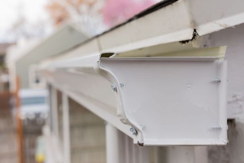 White metal gutter on a building eave with a bent corner, shot close-up outdoors.