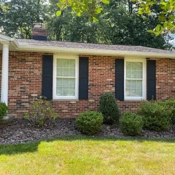 Brick house exterior with white-framed windows, black shutters, and a green front lawn