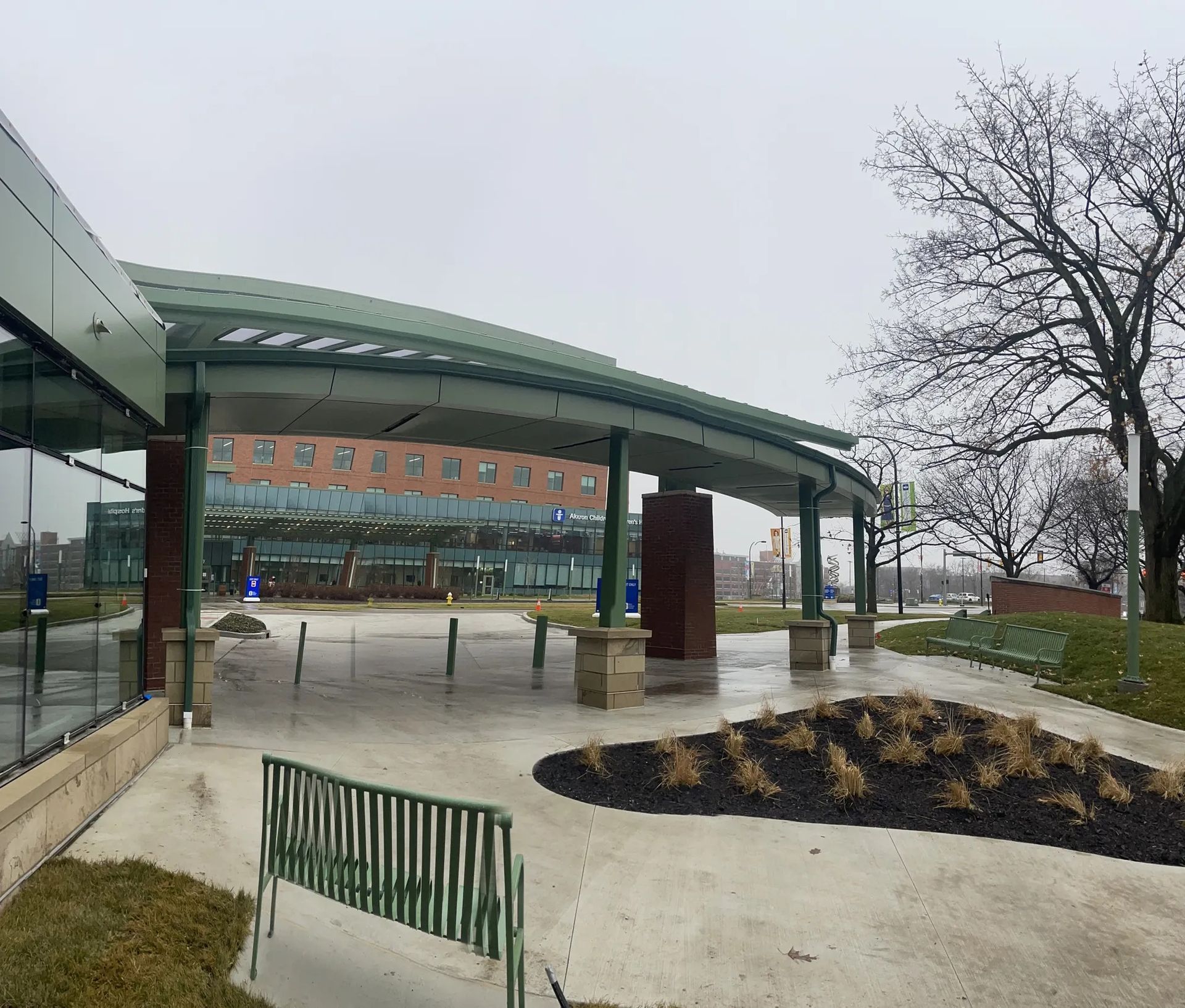 Rainy outdoor walkway beside a curved canopy, brick building, and bare trees.