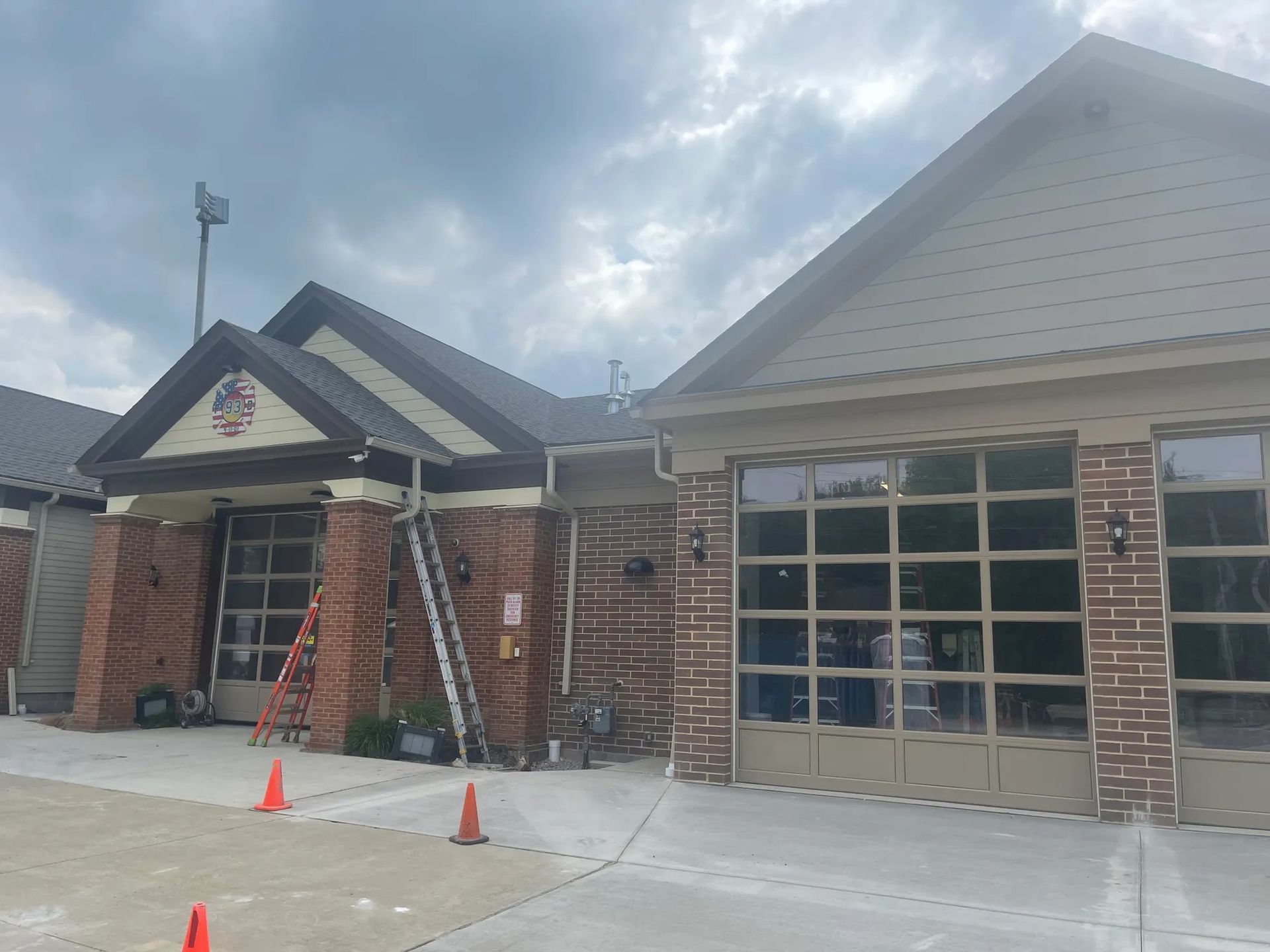 Brick house exterior with garage and front porch under cloudy sky, two orange cones on driveway
