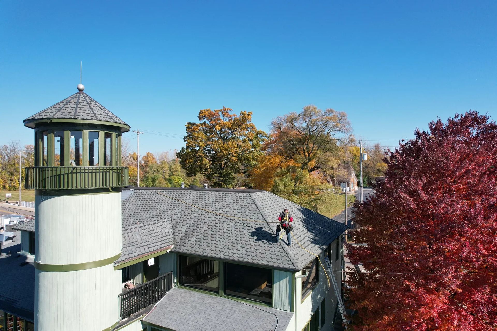A rooftop building with a small tower, framed by autumn trees under a clear blue sky.
