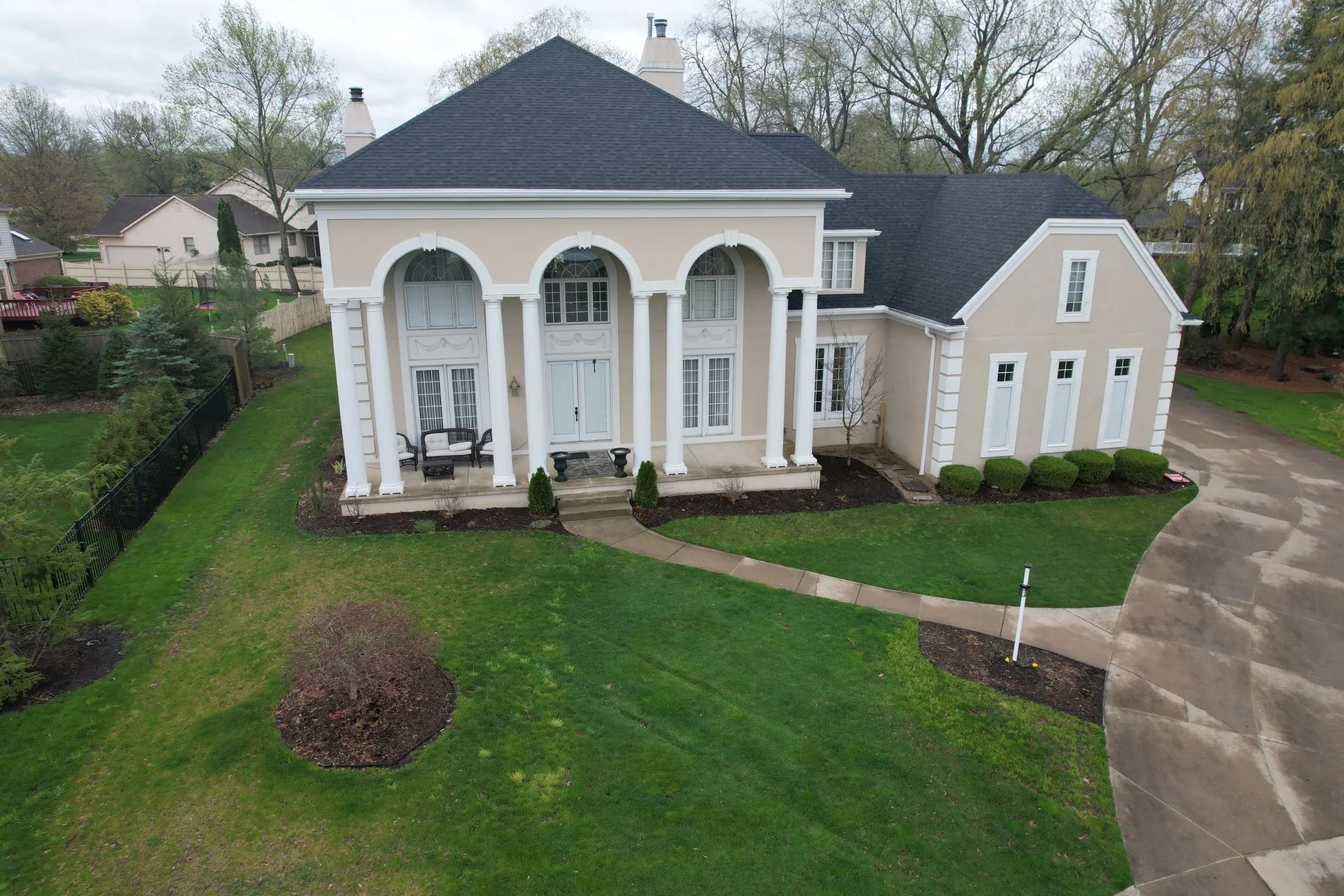 Large white house with columns, arched windows, and a driveway on a grassy lot