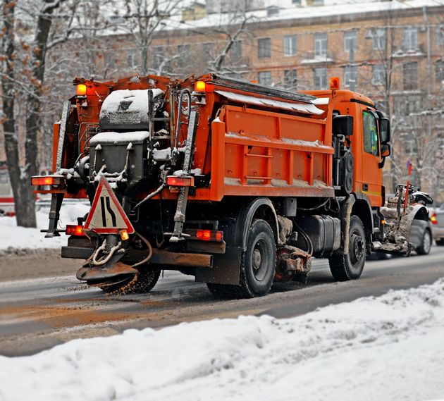 Orange snowplow truck clearing a snowy city street in winter