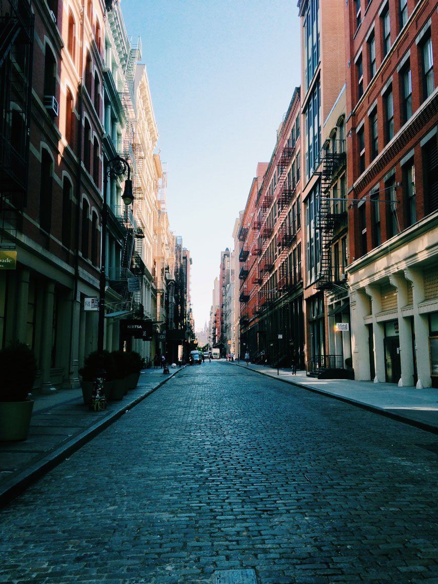 Empty cobblestone street lined with tall brick buildings on a city block.