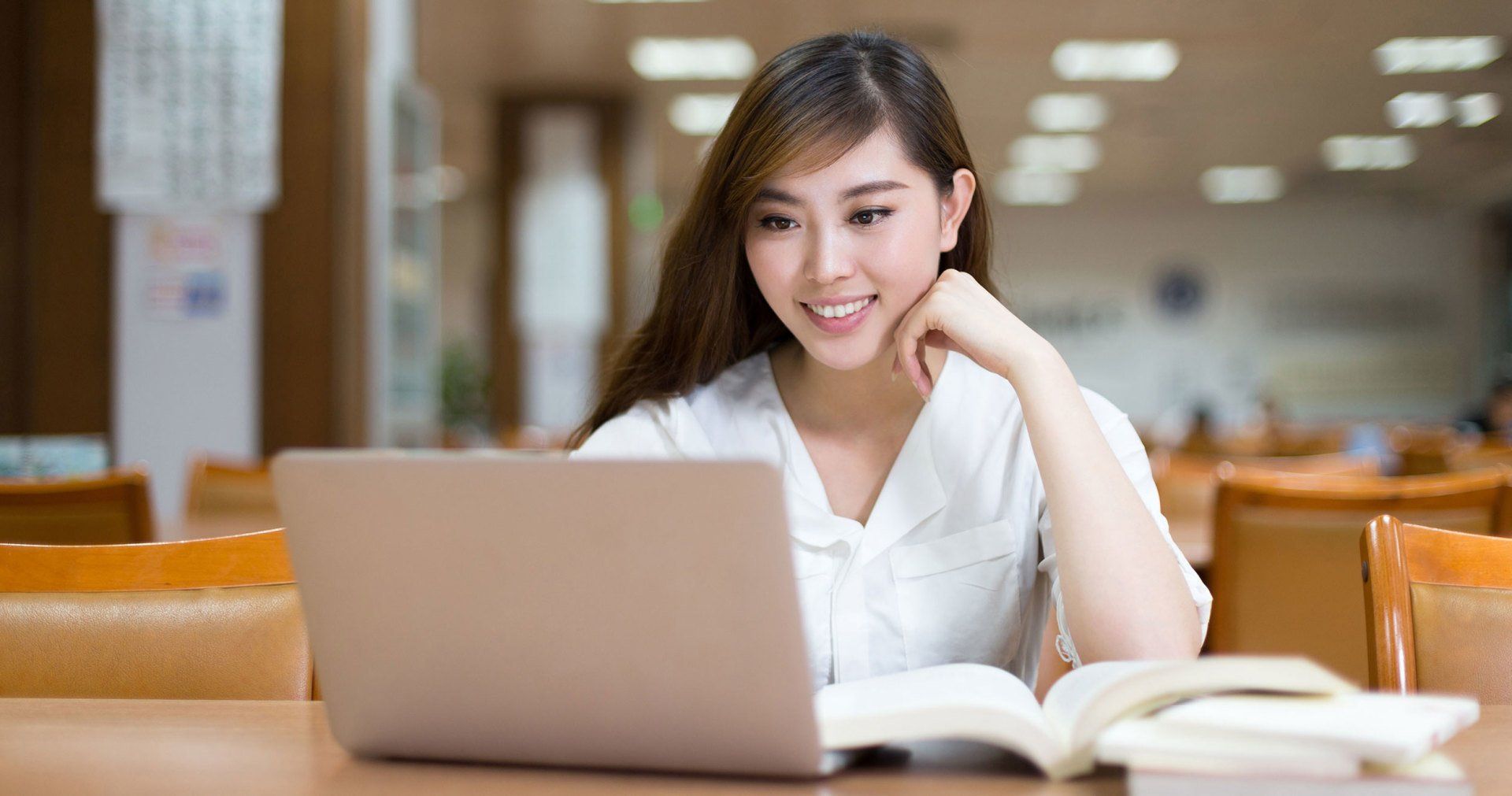 A woman is sitting at a table with a laptop and a book.