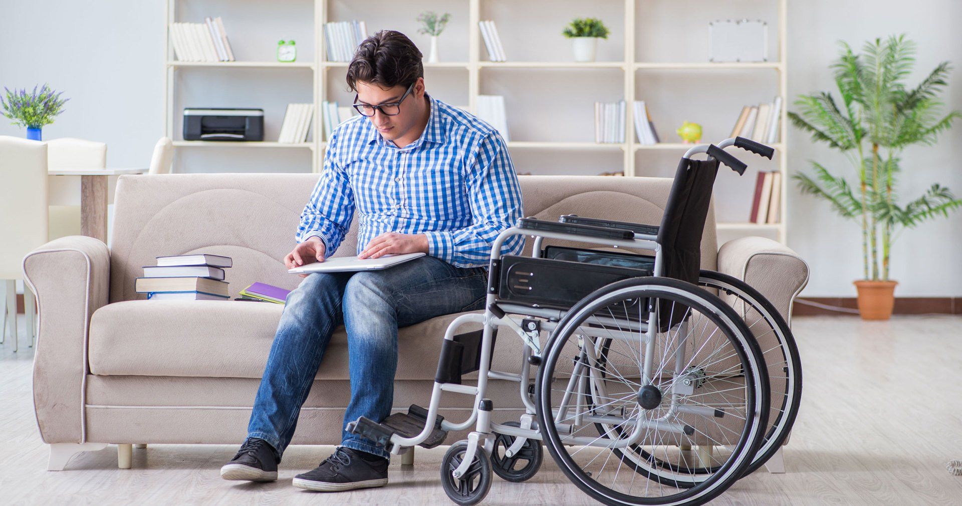 A man in a wheelchair is sitting on a couch using a laptop.