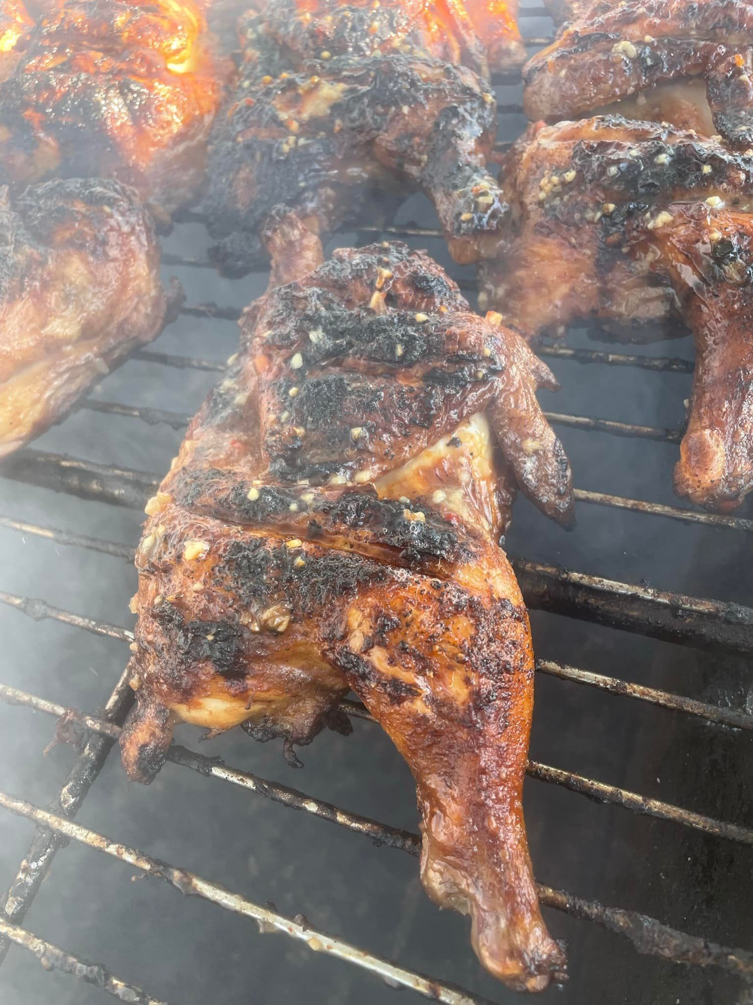 Chicken is being cooked on a grill with smoke coming out of it.