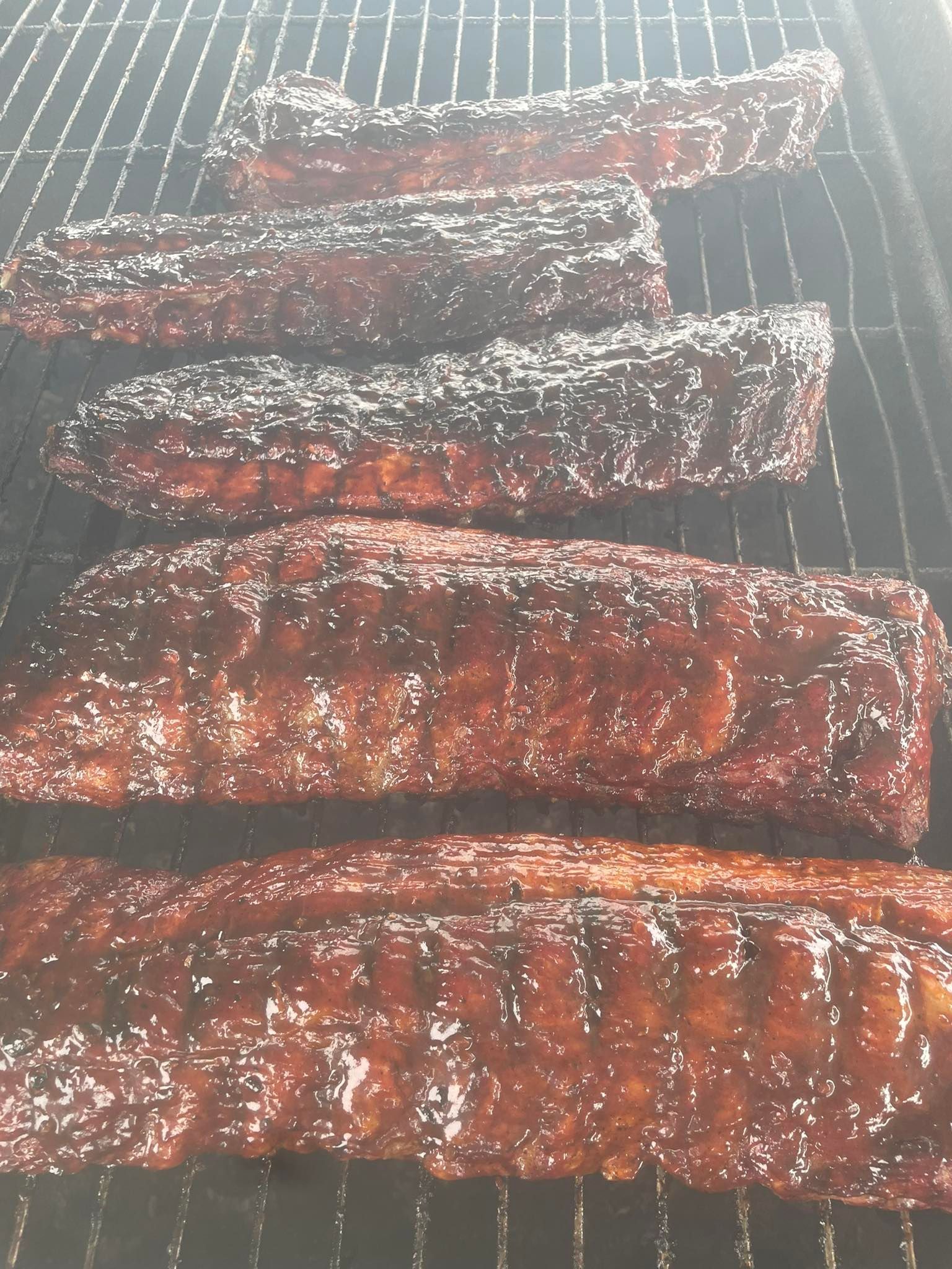 Ribs are being cooked on a grill and covered in sauce