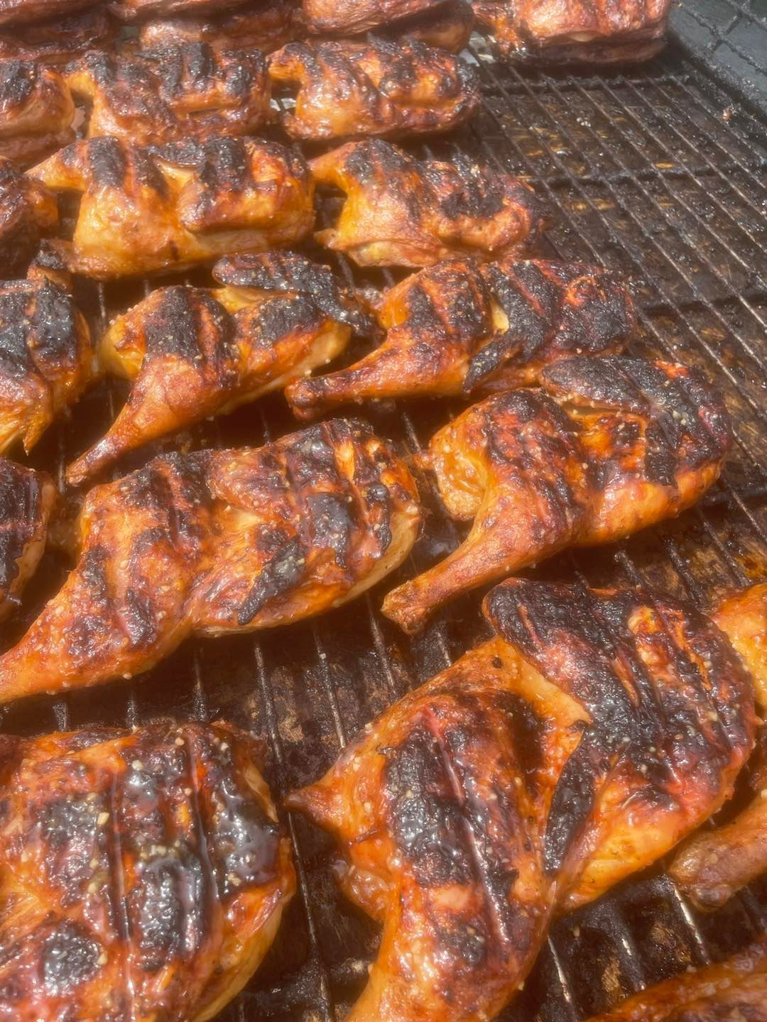 A bunch of chicken is cooking on a grill.