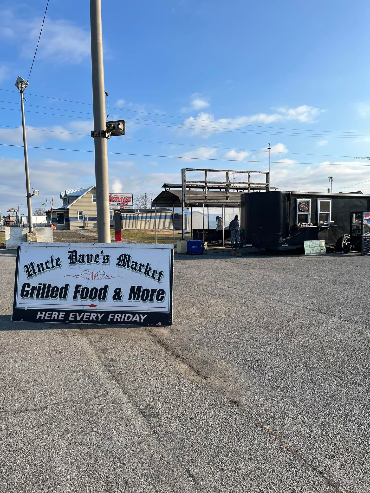 A sign in a gravel parking lot advertising grilled food and beer.