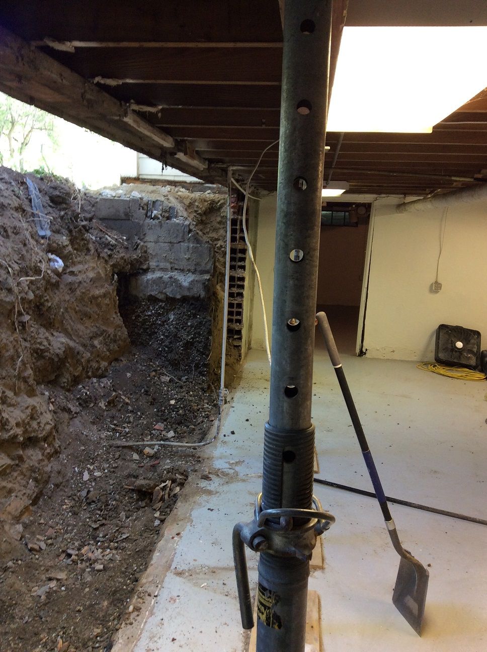 A shovel is sitting on a metal pole in a basement.