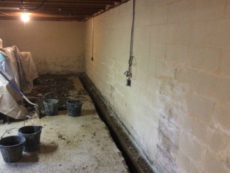 A basement with buckets and a broom on the floor.