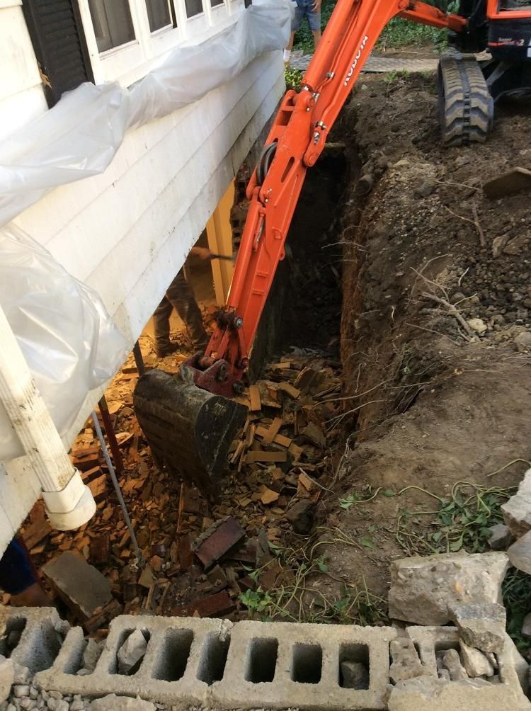 An excavator is digging a hole in the ground next to a house.