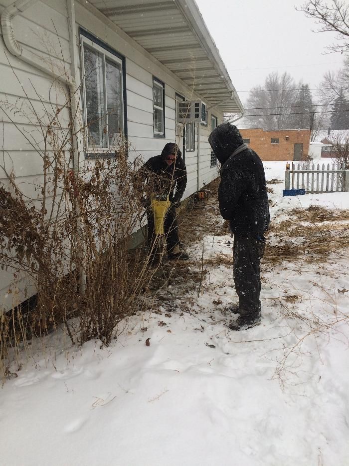 Two men are standing in the snow in front of a house.
