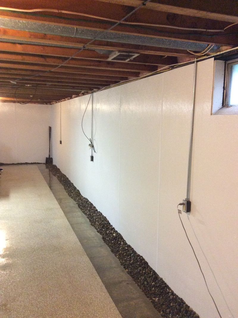 A basement with a long white wall and a window.