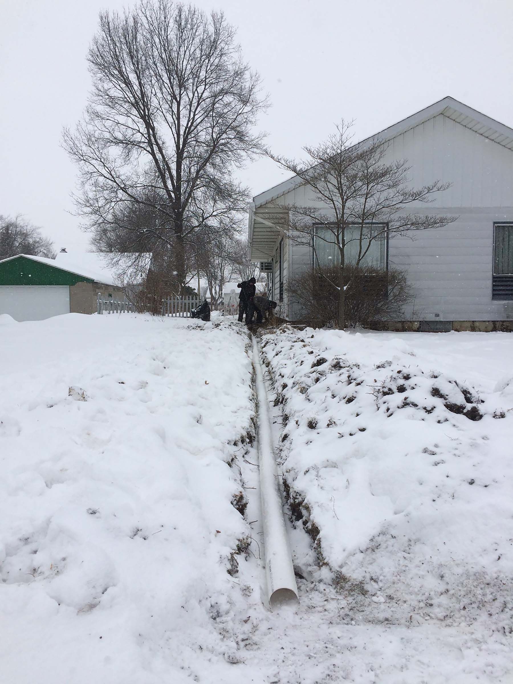 A pipe is laying in the snow in front of a house.