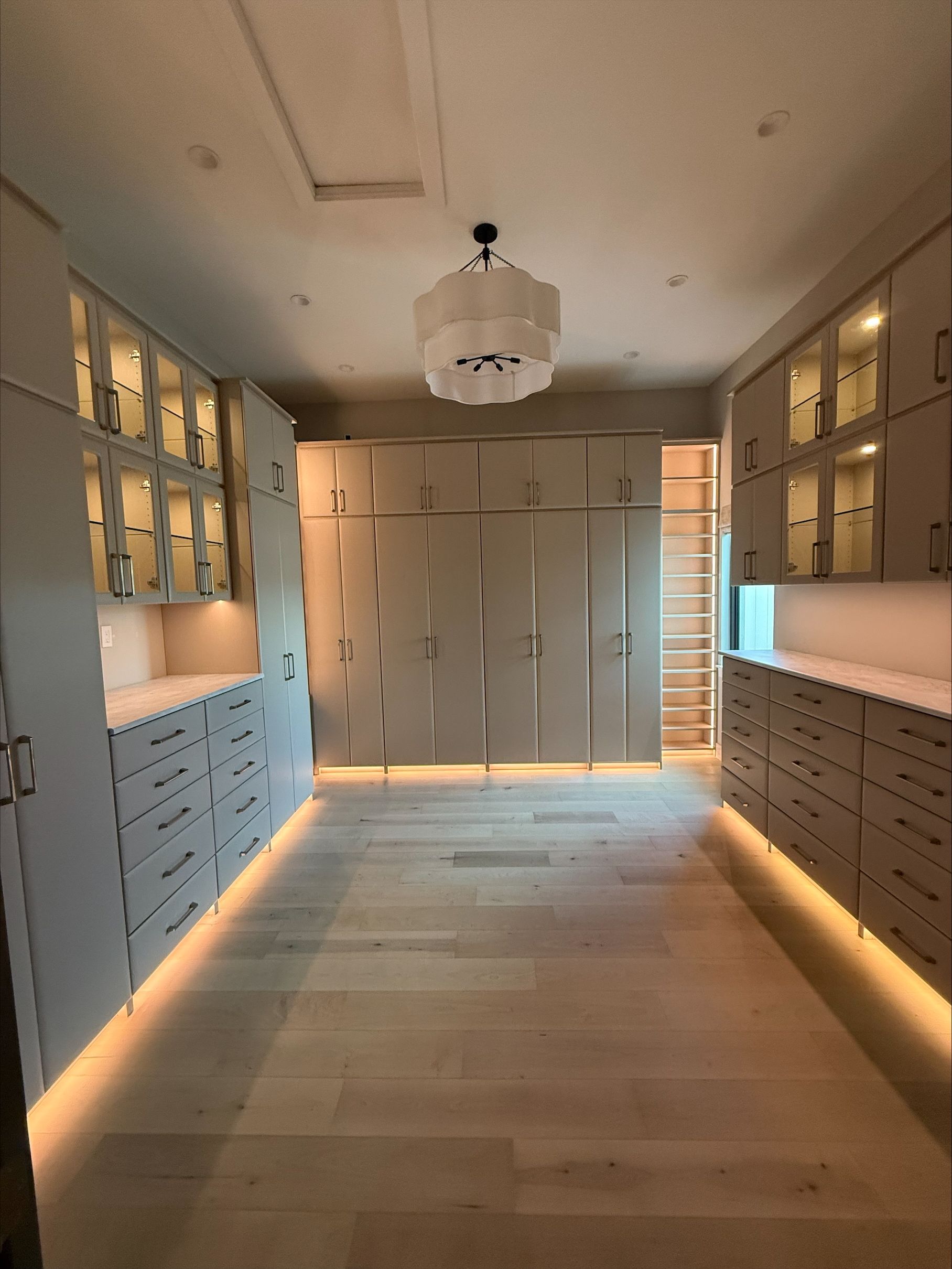 A large, luxurious walk-in closet with light-colored cabinets, wooden floors, and a chandelier.