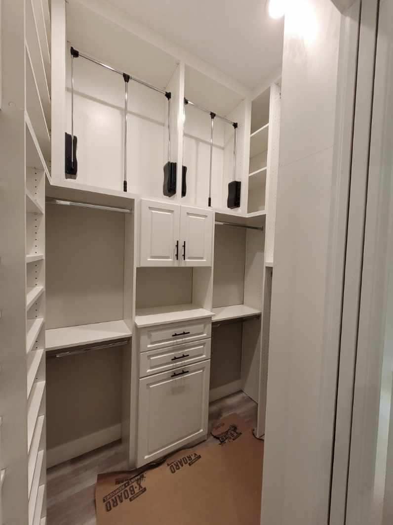 A walk in closet with white cabinets , shelves and drawers.
