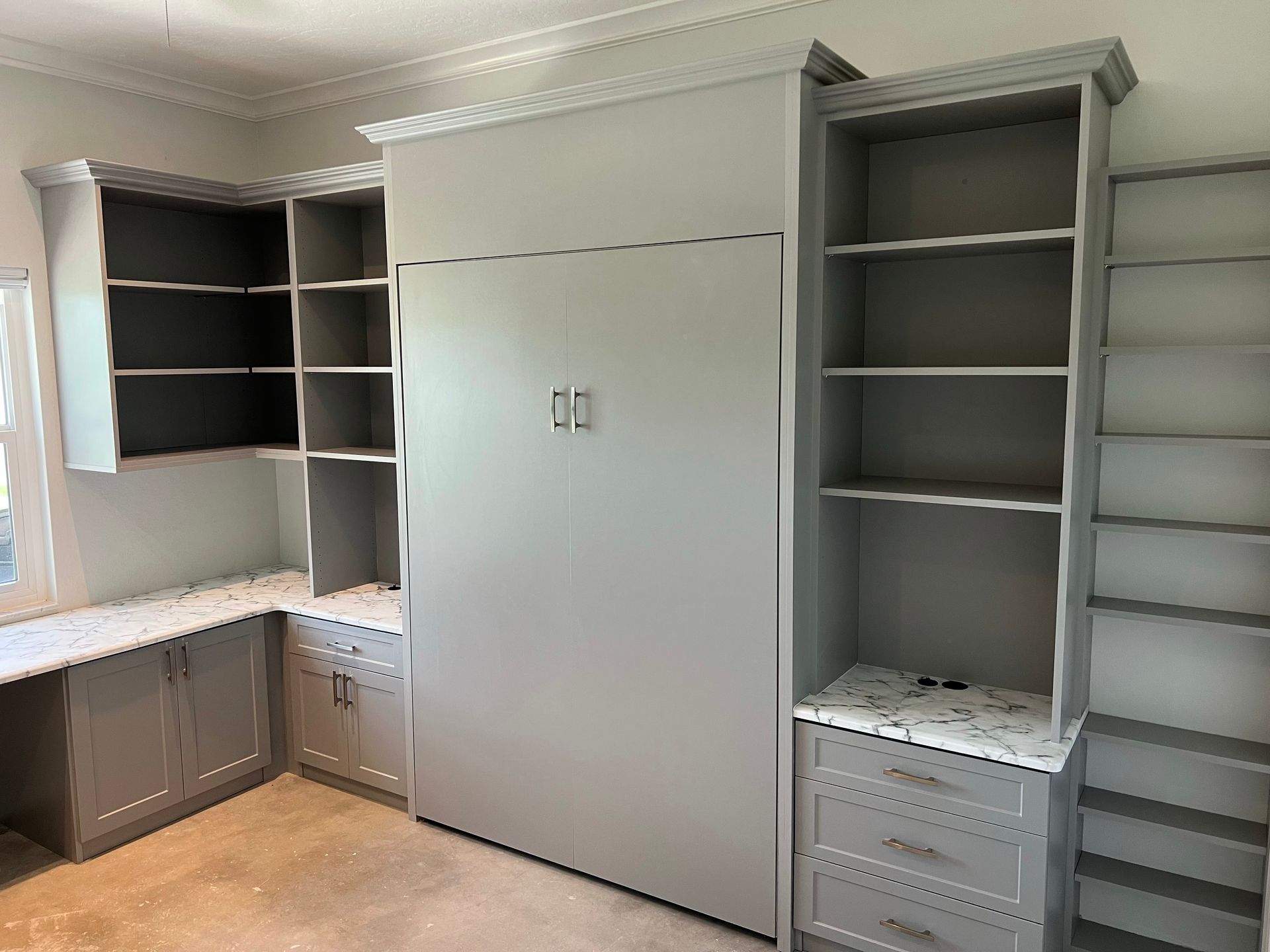 A bedroom with a wall bed, shelves, cabinets, and a desk.