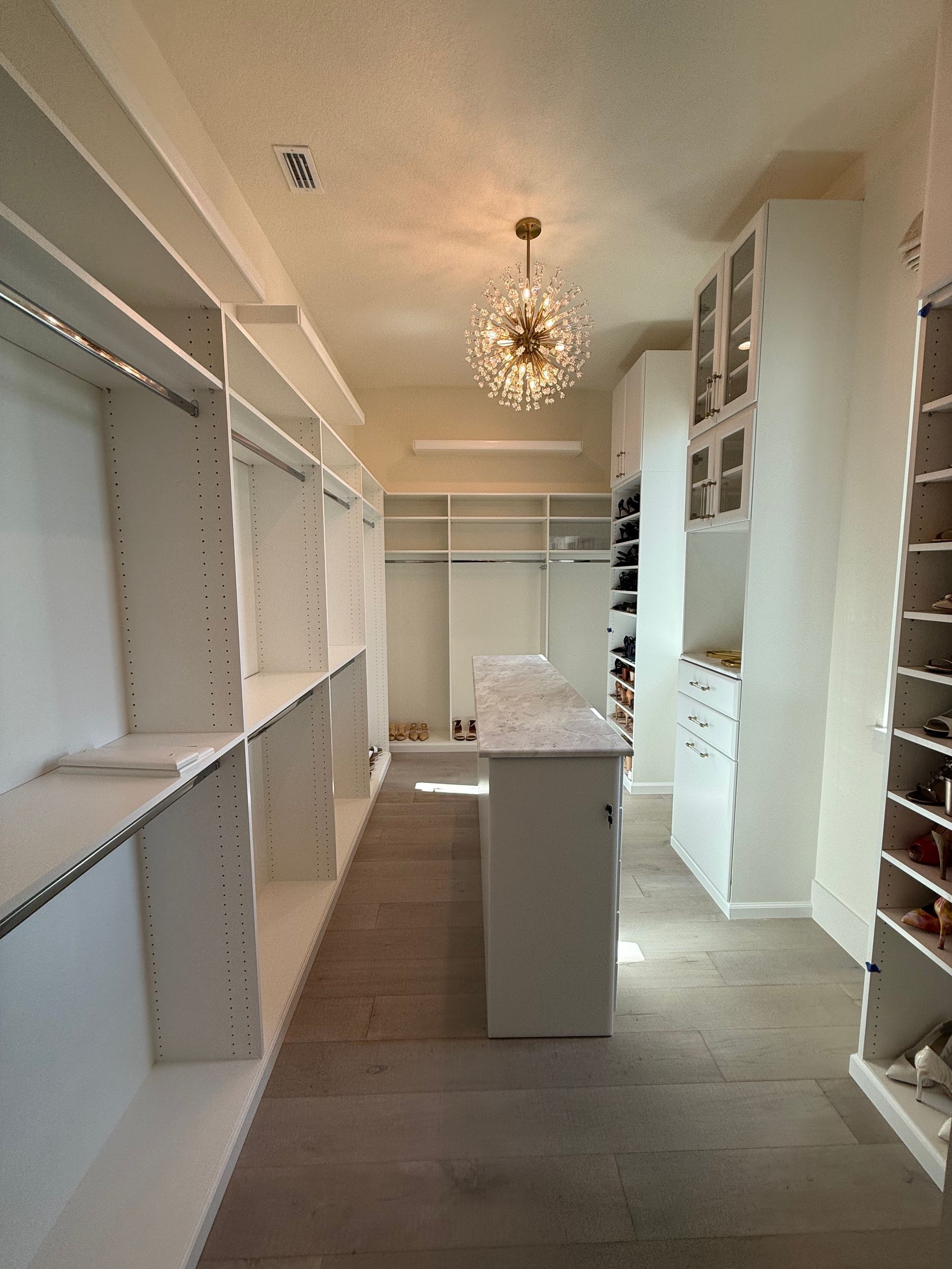 A walk in closet with lots of shelves and a chandelier hanging from the ceiling.