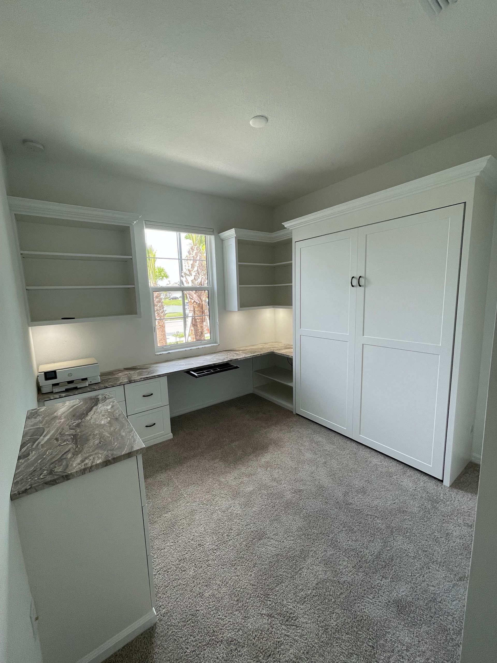 A room with a desk , cabinets , shelves and a window.