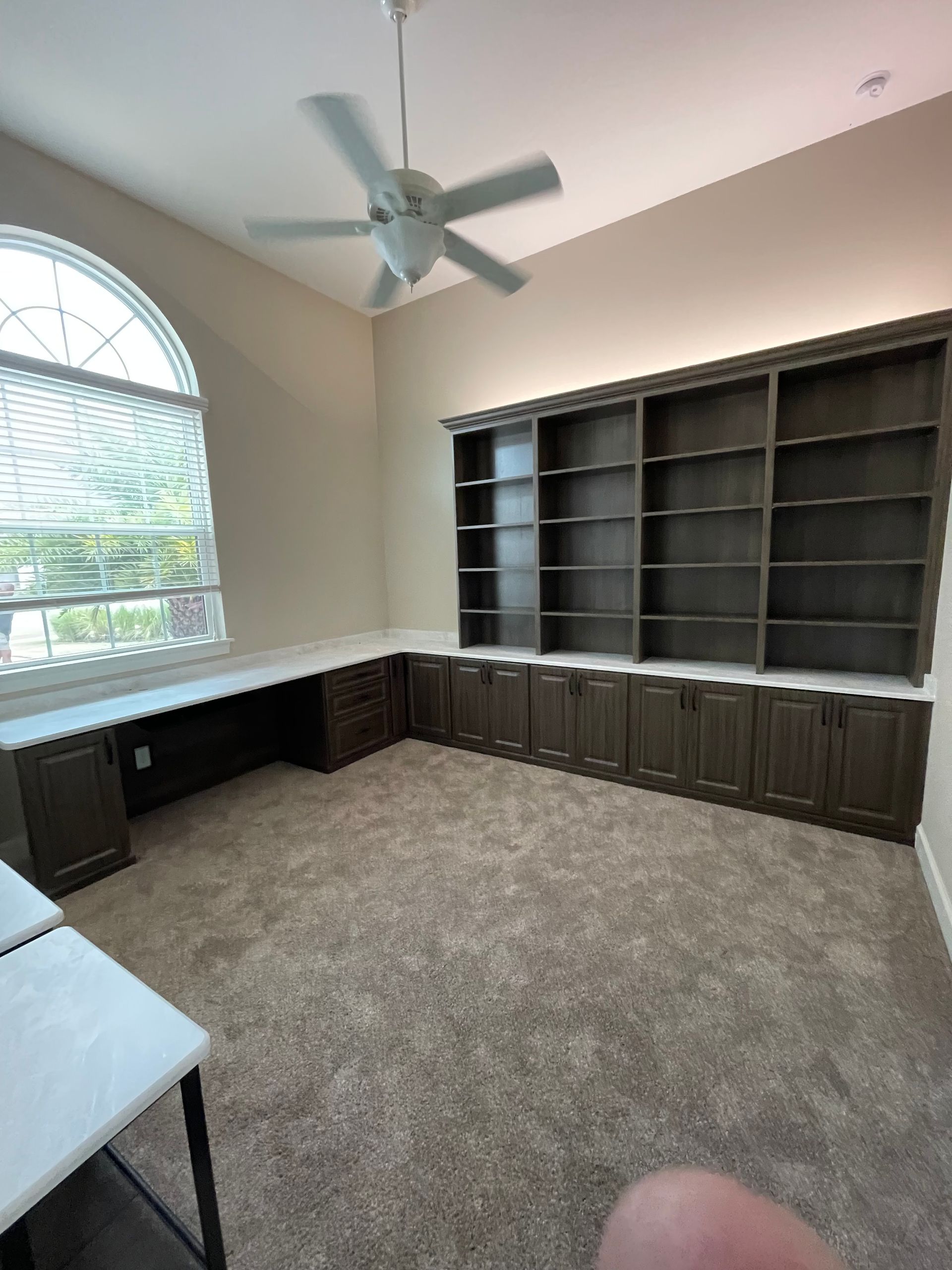There is a ceiling fan in the room with a lot of shelves.