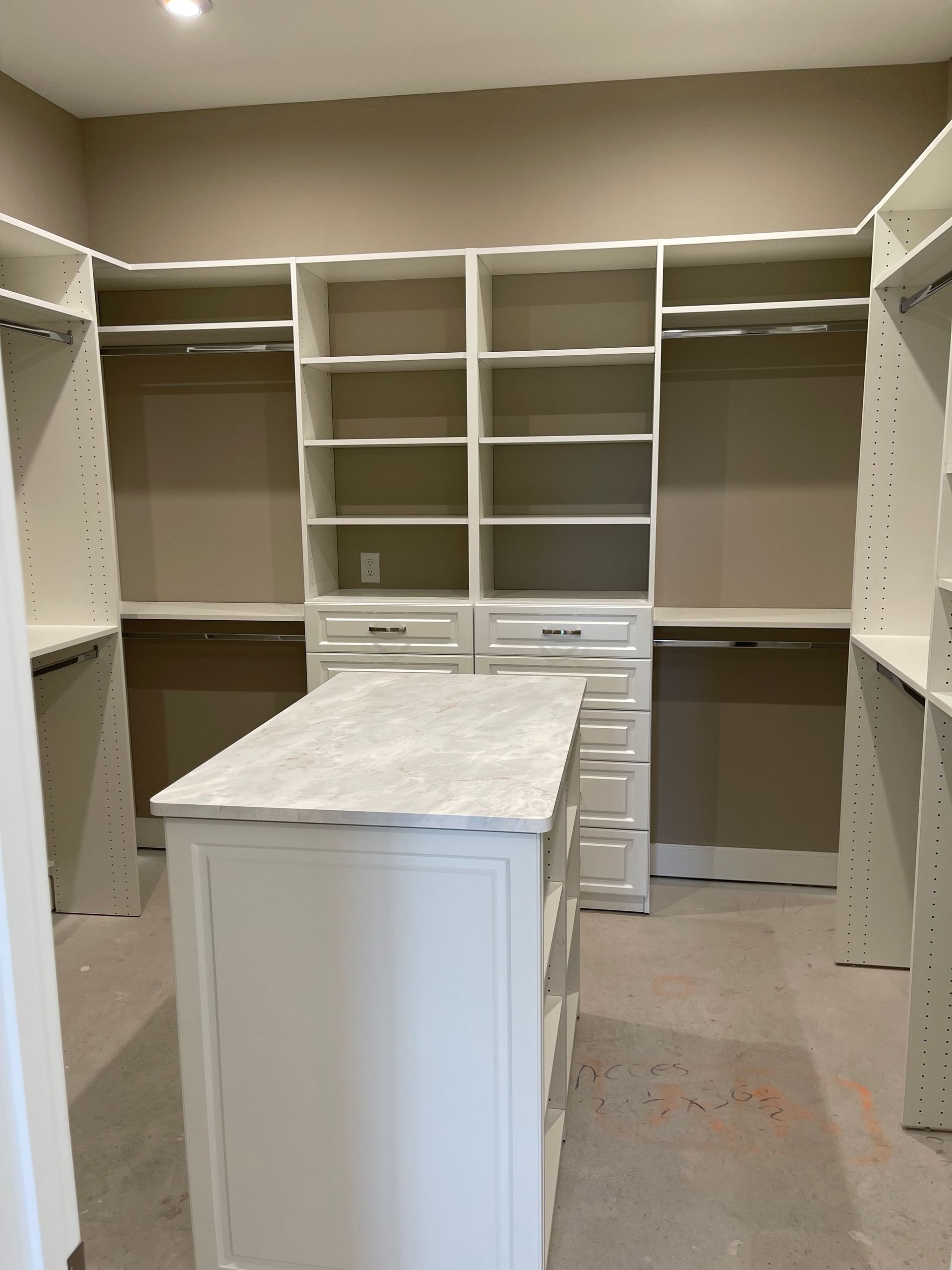 A walk in closet with lots of shelves and drawers and a large island in the middle.