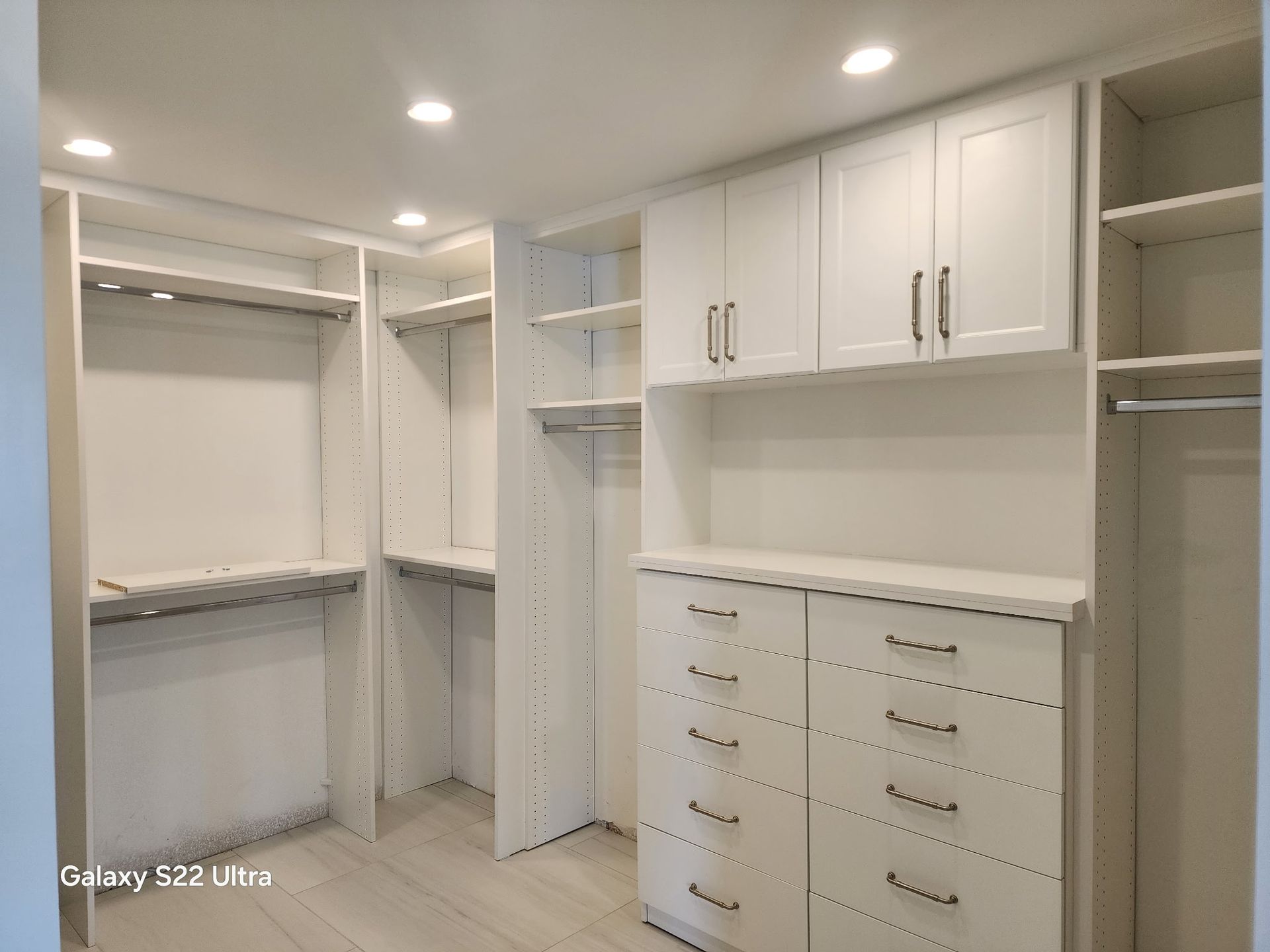 A walk in closet with white cabinets and drawers.
