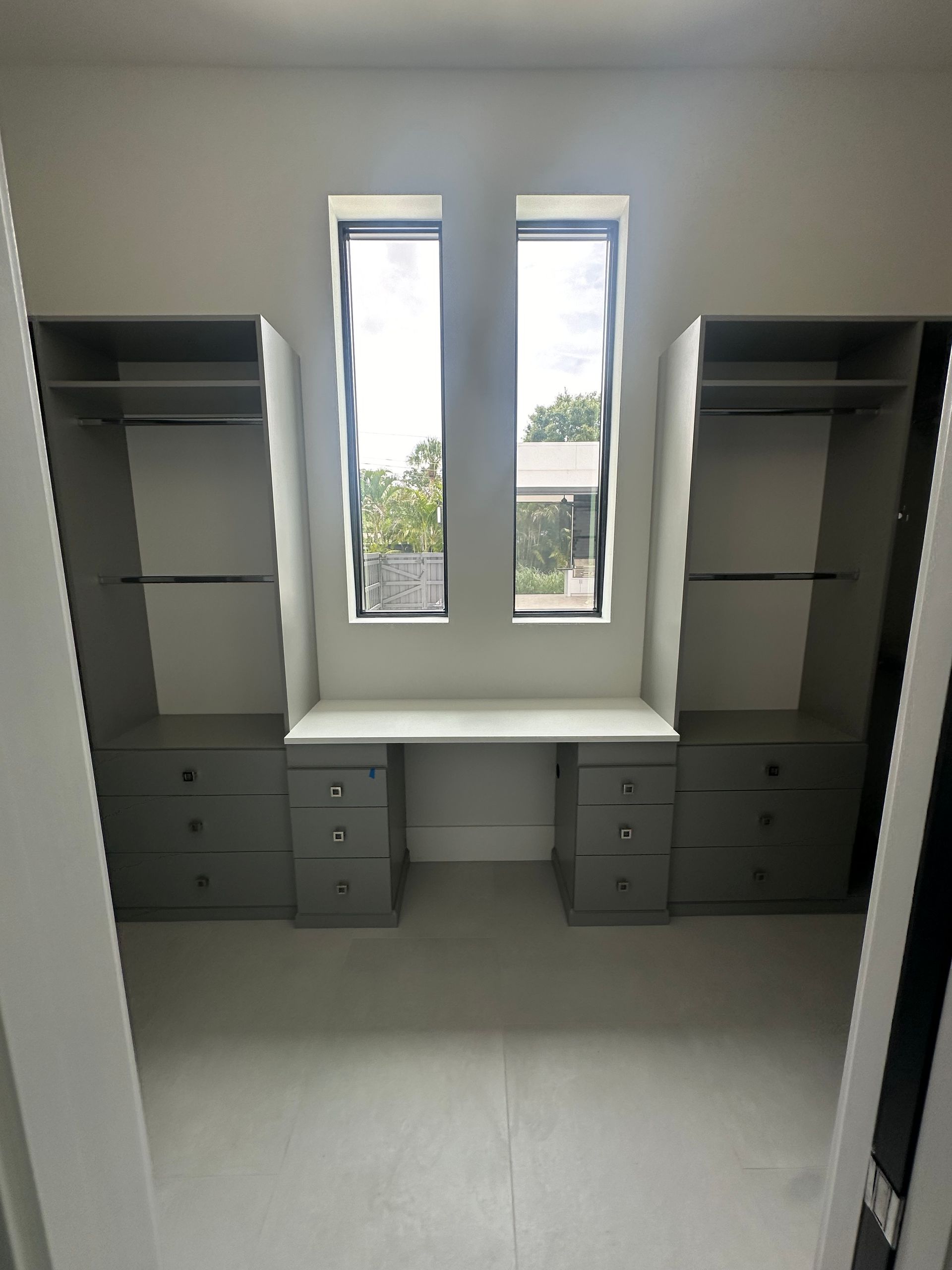 A walk in closet with a desk and two windows.