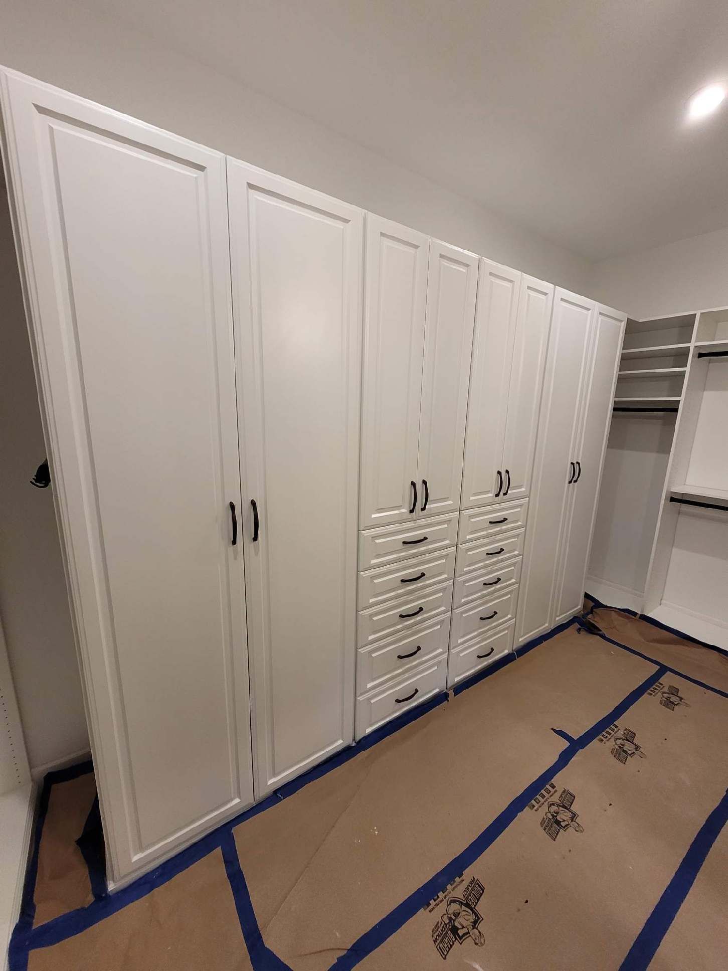 A walk in closet with lots of white cabinets and drawers.