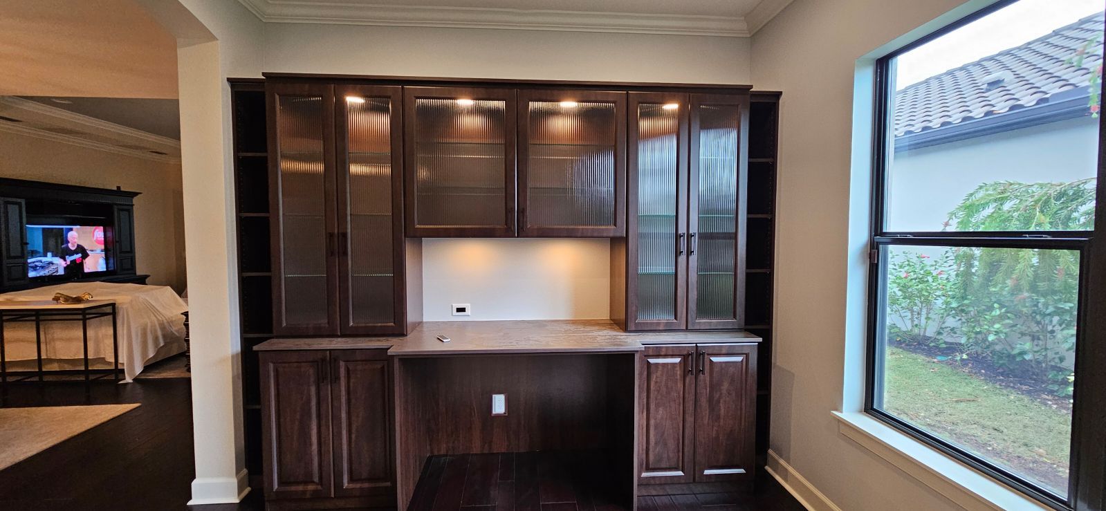 A room with a desk, cabinets, shelves, and a window.