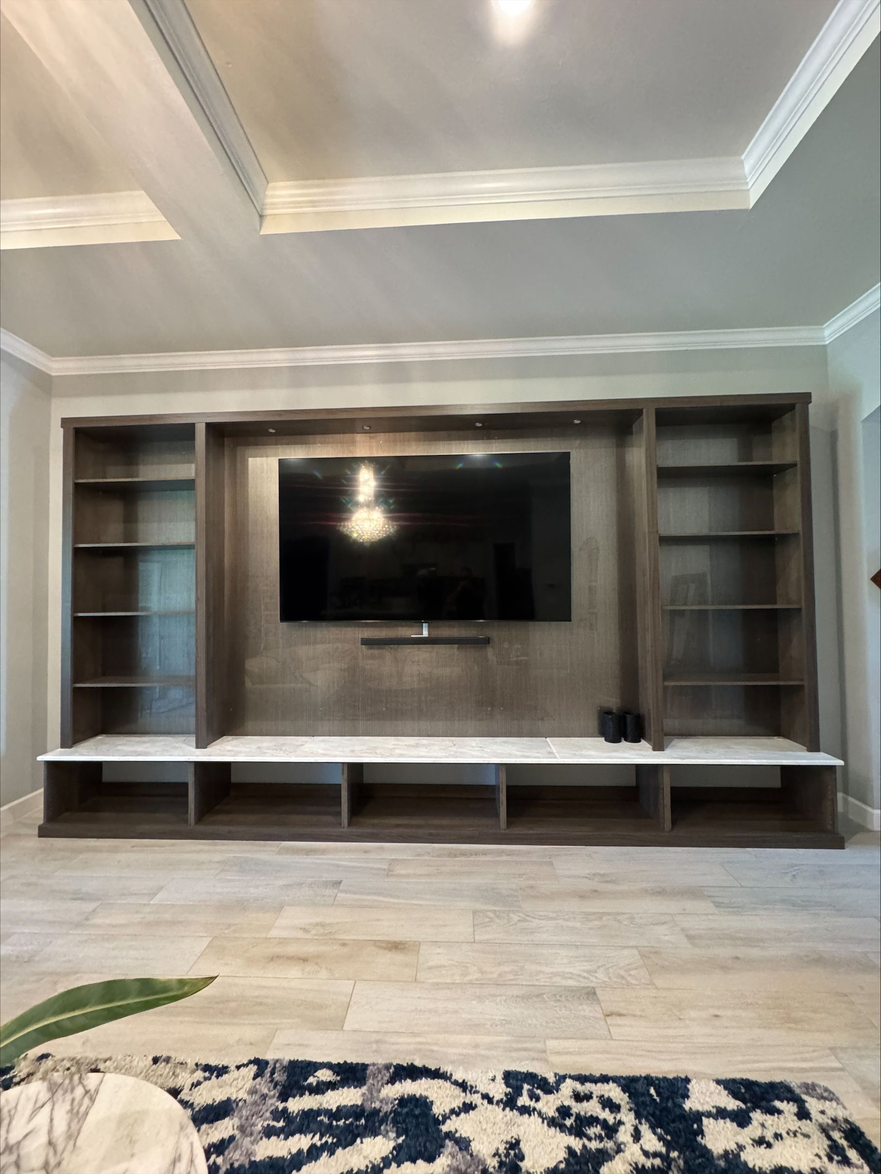Built-in entertainment center: gray shelving and cabinets, a large TV, and marble-like countertop.