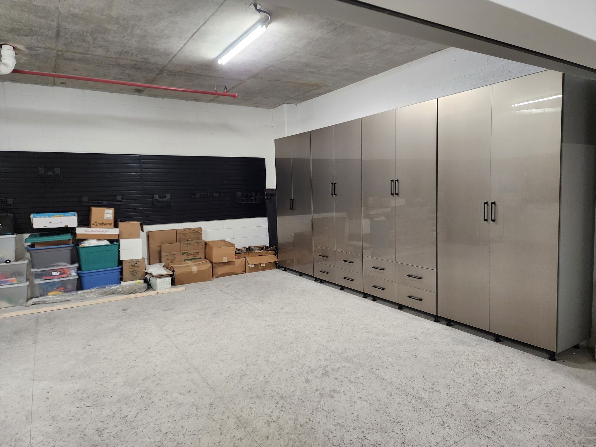 Garage interior with a row of tall, metallic storage cabinets next to a black slat wall and various cardboard boxes. 