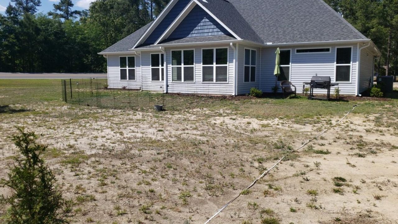 A white house with a gray roof is sitting in the middle of a dirt field.