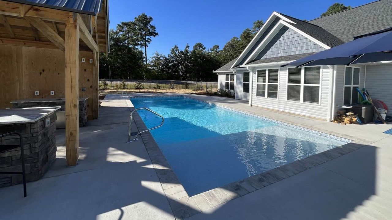A large swimming pool is in the backyard of a house.