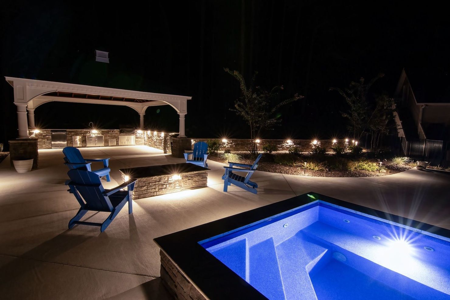 A patio with a gazebo , chairs , and a pool at night.