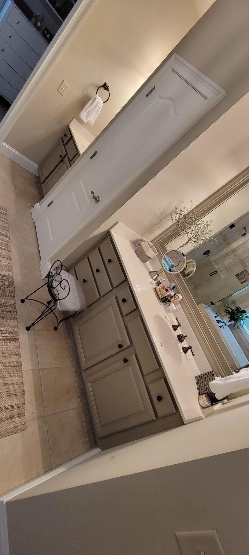 Rotated photo of a bathroom vanity with mirror, cabinets, and beige tile walls.