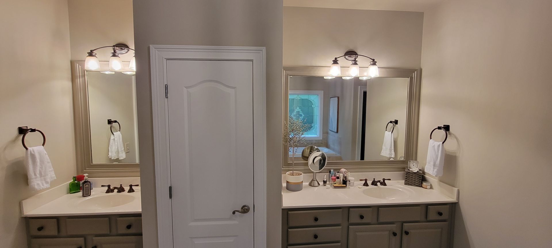 Bathroom vanity with mirror, sink, white cabinets, and a centered door between two matching sinks.