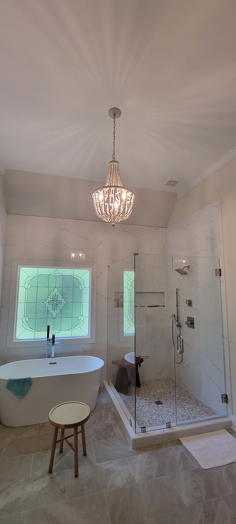 Bright bathroom with chandelier, freestanding tub, walk-in shower, and window light.
